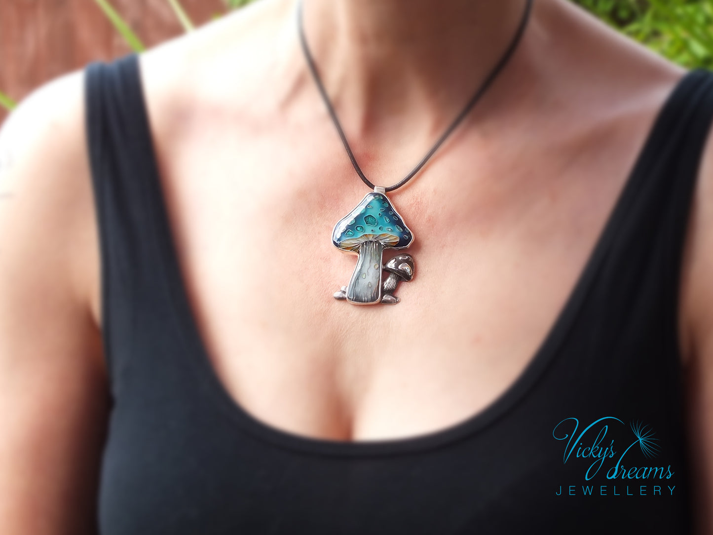 Person wearing a black tank top with a unique mushroom-shaped pendant necklace.