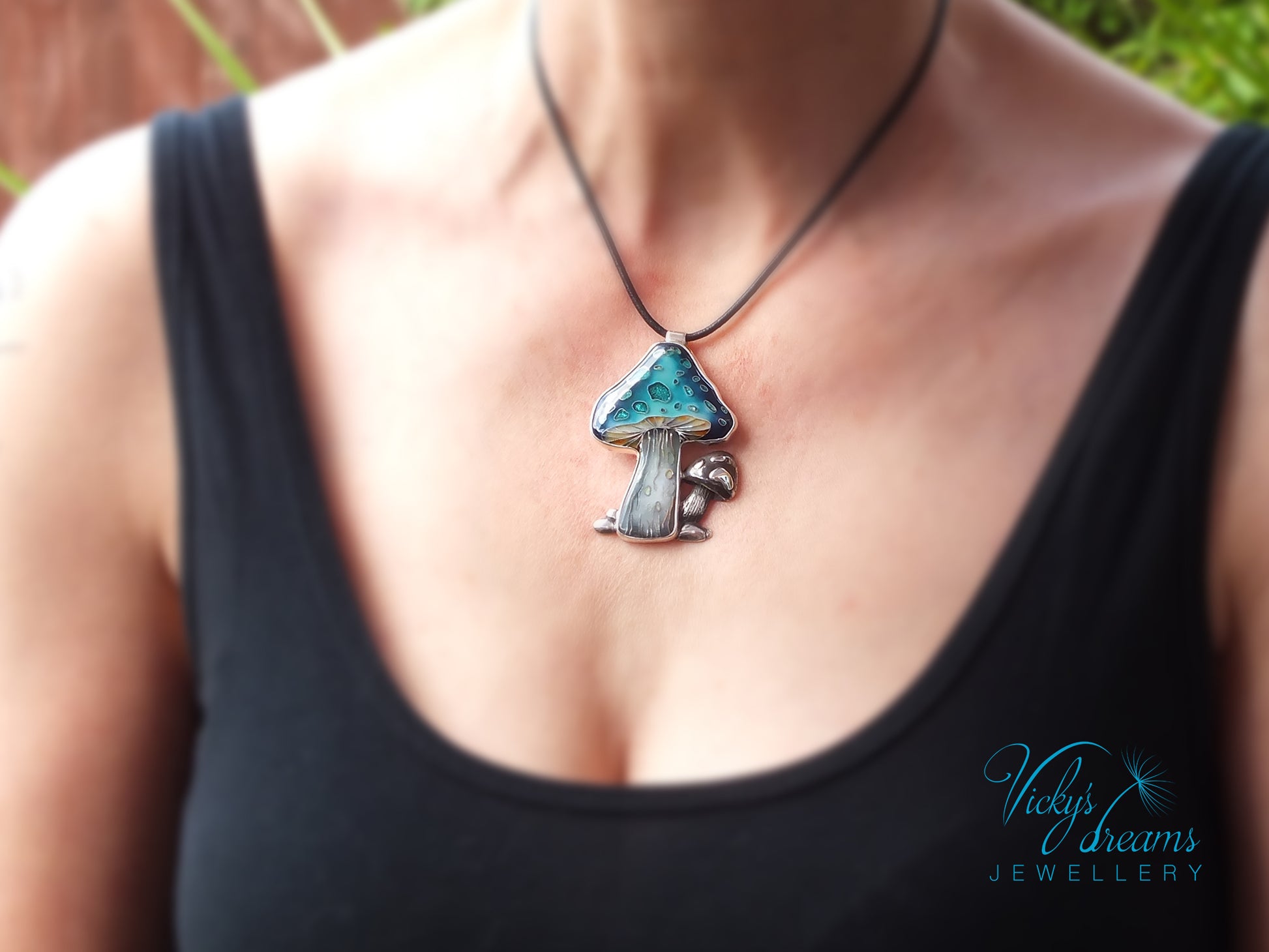 Person wearing a black tank top with a unique mushroom-shaped pendant necklace.