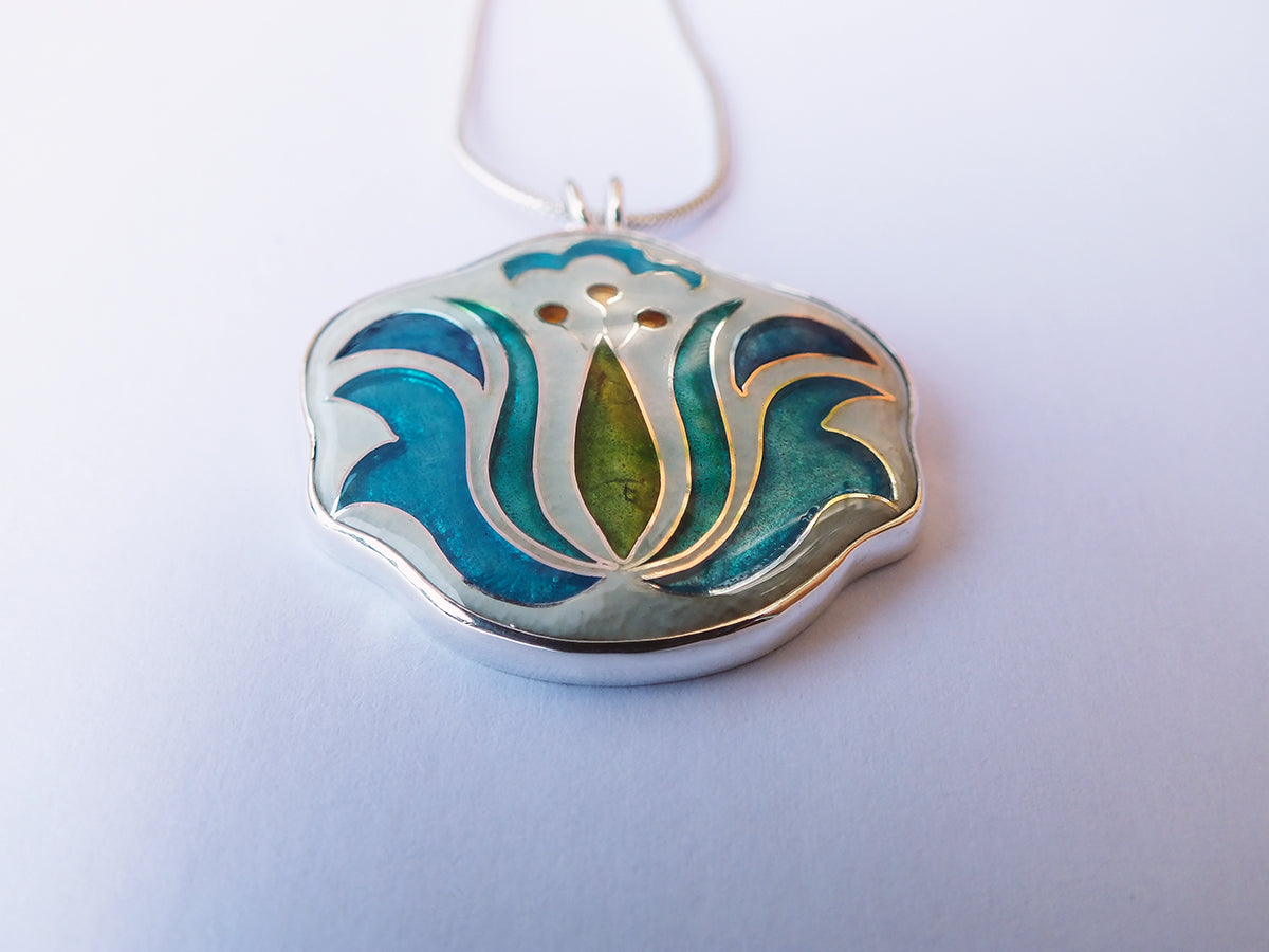 Silver pendant with blue and green design on a white background