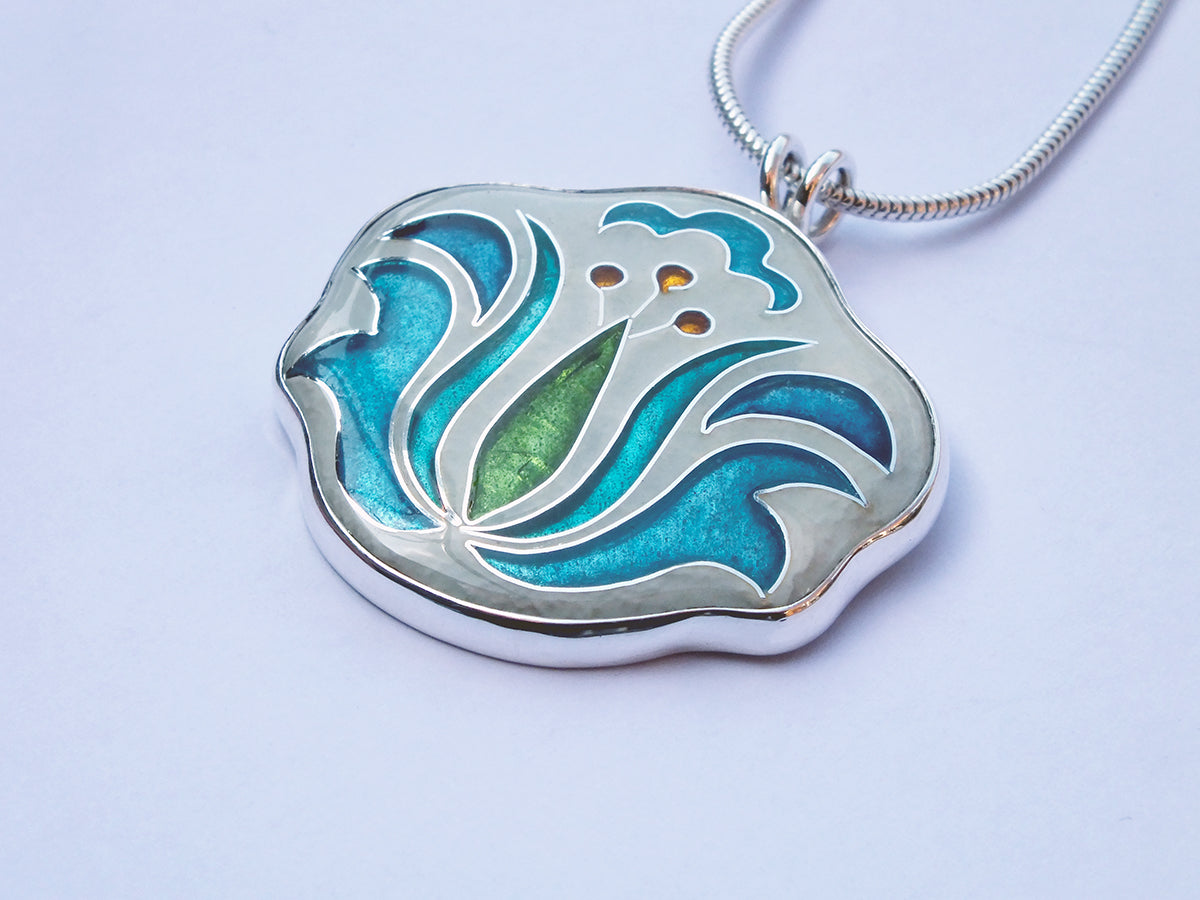 Silver pendant with blue and green design on a light purple background