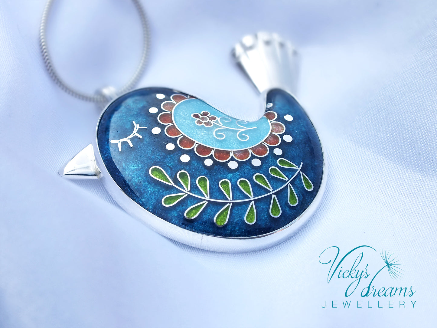 Decorative pendant with intricate designs on a blue background, featuring 'Vicky's Dreams Jewellery' logo.