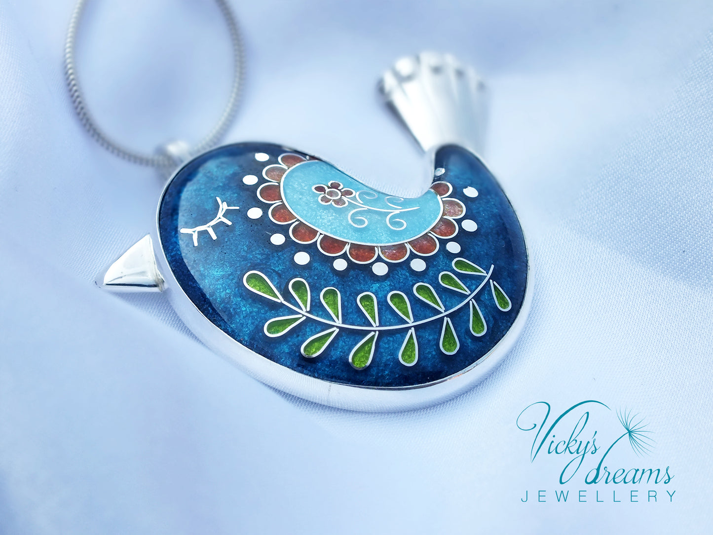 Decorative pendant with intricate designs on a blue background, featuring the brand 'Vicky's Dreams Jewellery'.