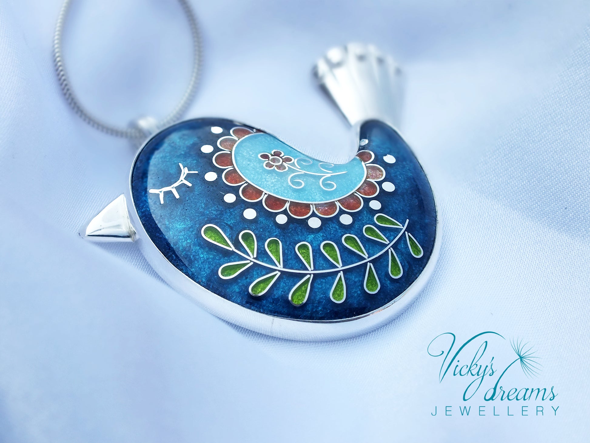 Decorative pendant with intricate designs on a blue background, featuring the brand 'Vicky's Dreams Jewellery'.