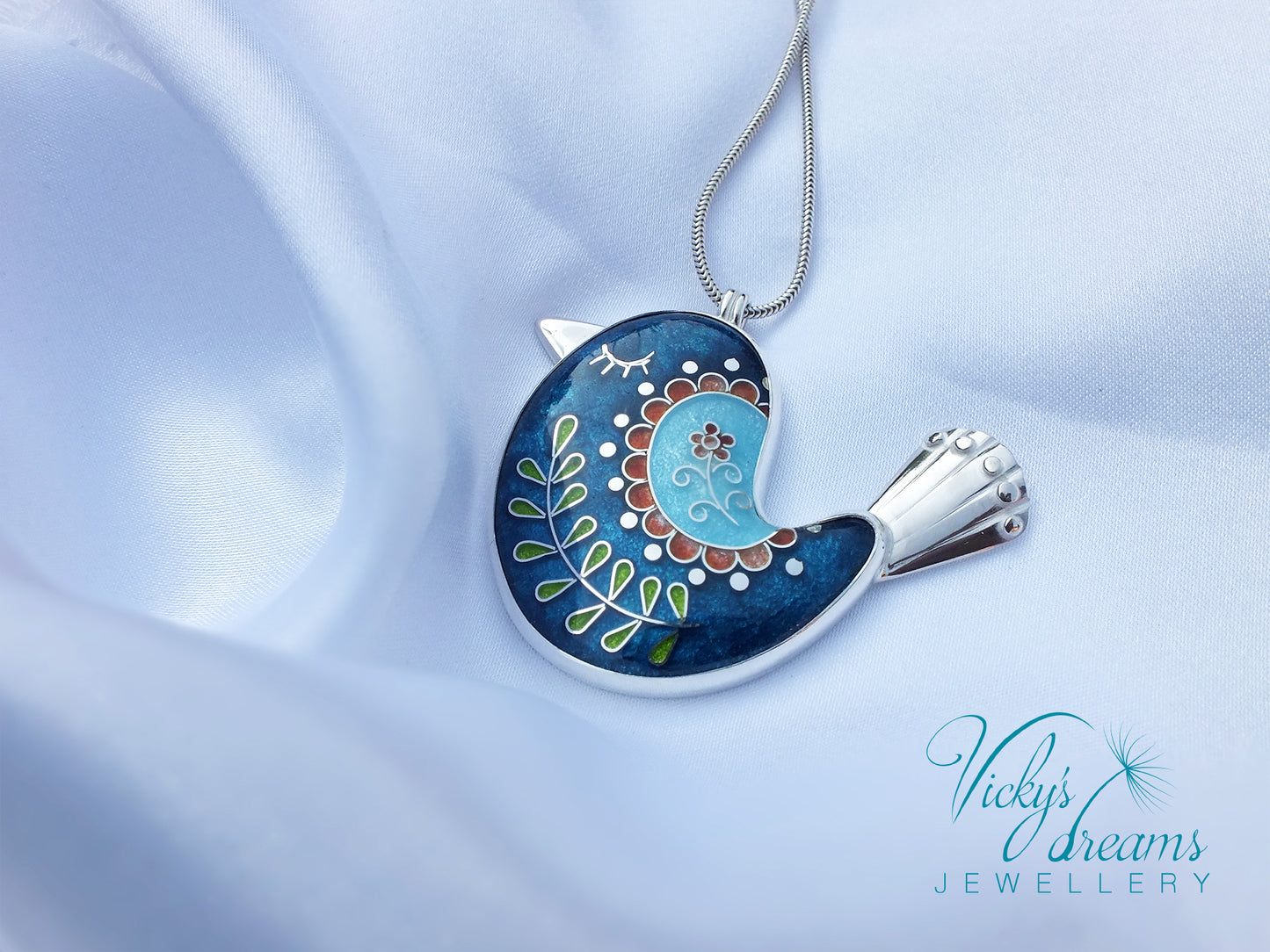 Decorative bird-shaped pendant on a light blue fabric background with 'Vicky's Dreams Jewellery' branding.