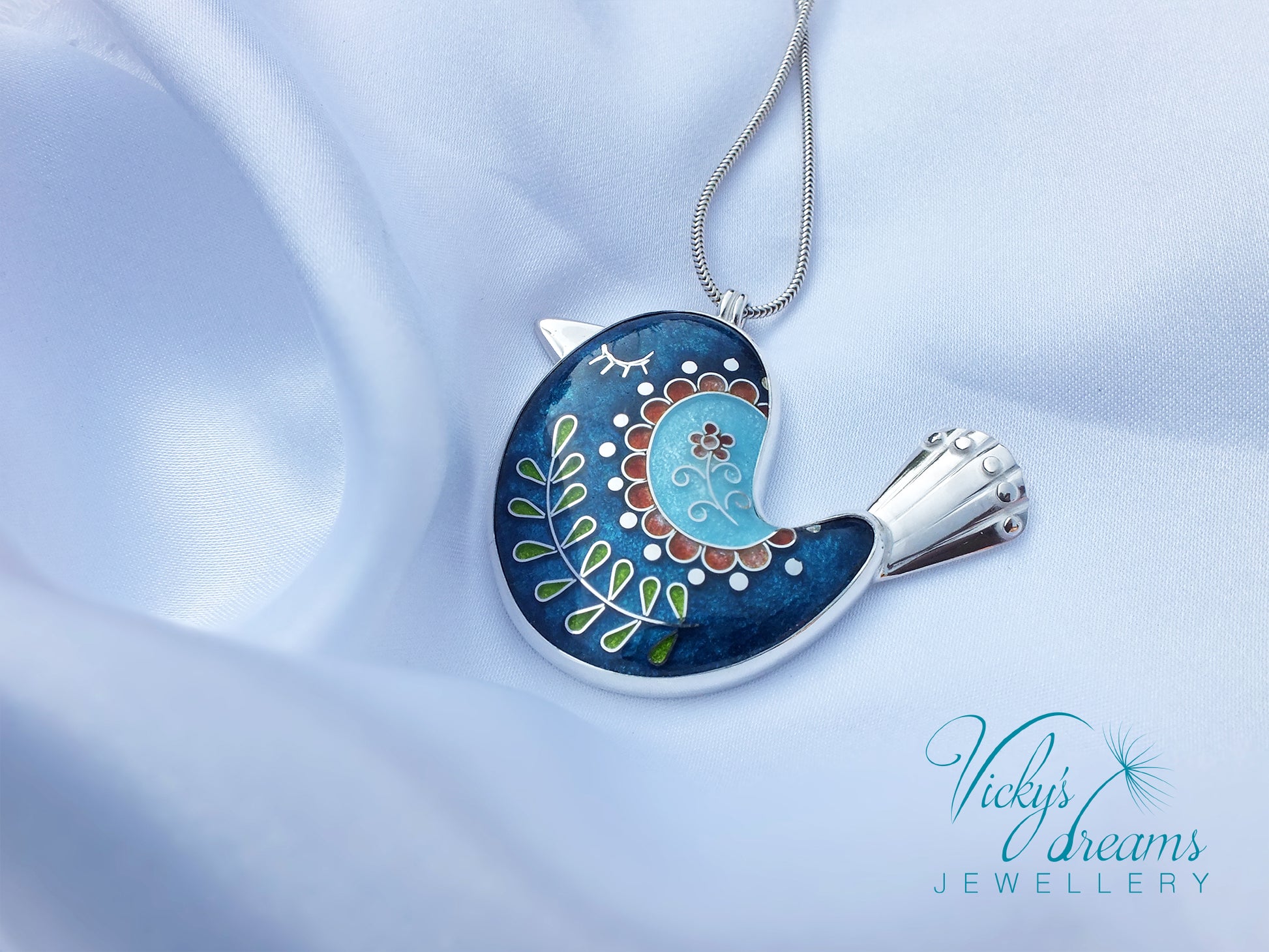 Decorative bird-shaped pendant on a light blue fabric background with 'Vicky's Dreams Jewellery' branding.