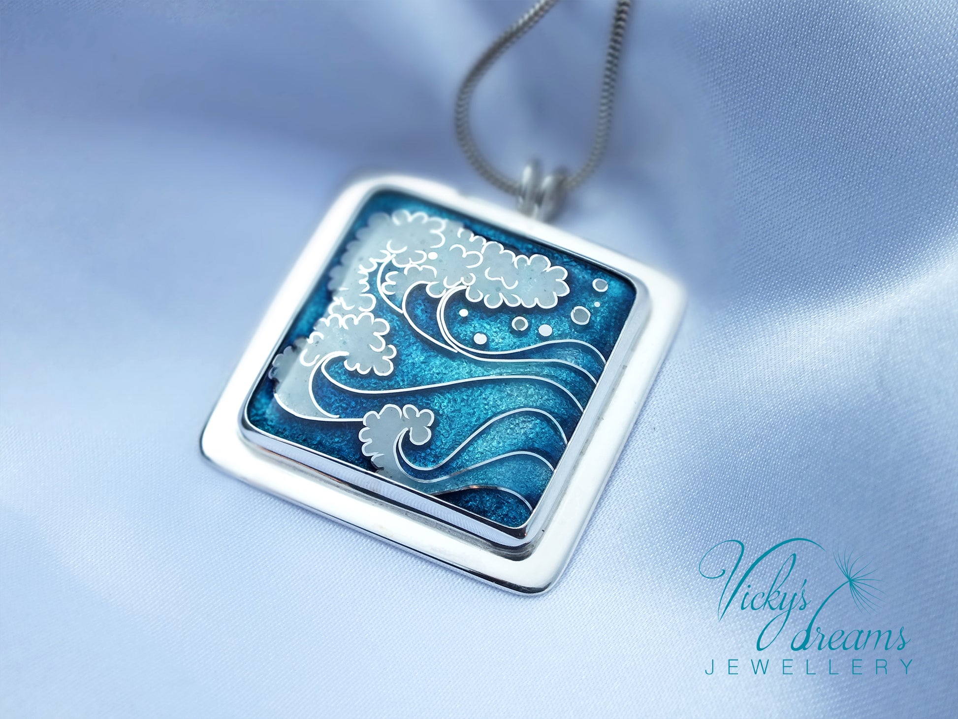 Silver pendant with wave design on a blue satin background, featuring 'Vicky's Dreams Jewellery'.
