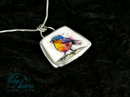 Handmade sterling silver pendant featuring a handpainted bird on a reclaimed porcelain fragment, with bright, joyful enamel colours and elegant silver frame