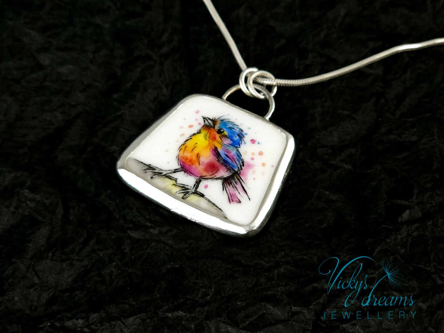 Handmade sterling silver pendant featuring a handpainted bird on a reclaimed porcelain fragment, with bright, joyful enamel colours and elegant silver frame