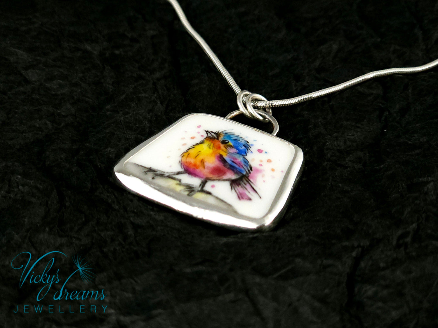 Handmade sterling silver pendant featuring a handpainted bird on a reclaimed porcelain fragment, with bright, joyful enamel colours and elegant silver frame