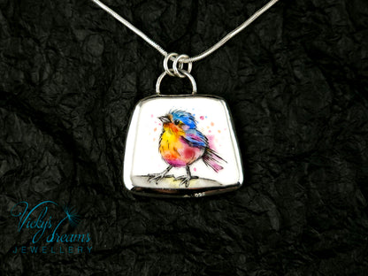 Handmade sterling silver pendant featuring a handpainted bird on a reclaimed porcelain fragment, with bright, joyful enamel colours and elegant silver frame