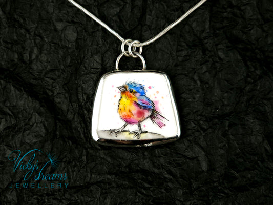Handmade sterling silver pendant featuring a handpainted bird on a reclaimed porcelain fragment, with bright, joyful enamel colours and elegant silver frame
