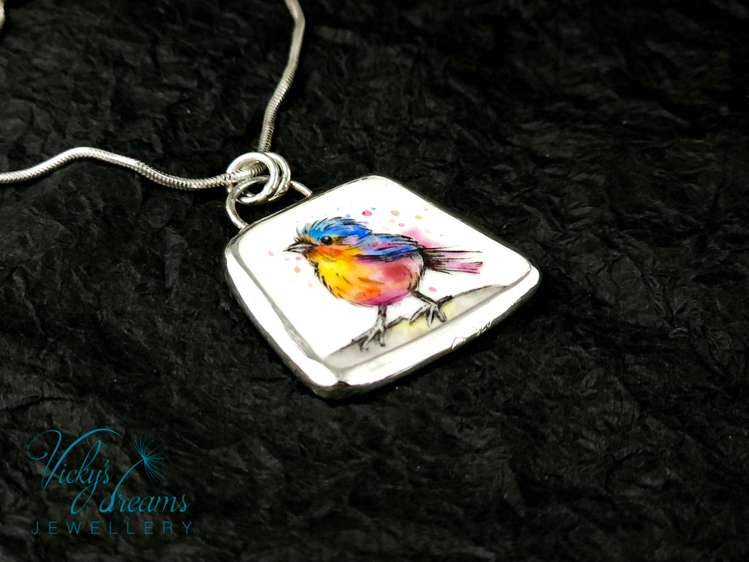 Handmade sterling silver pendant featuring a handpainted bird on a reclaimed porcelain fragment, with bright, joyful enamel colours and elegant silver frame