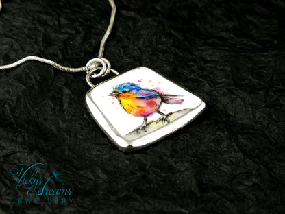 Handmade sterling silver pendant featuring a handpainted bird on a reclaimed porcelain fragment, with bright, joyful enamel colours and elegant silver frame