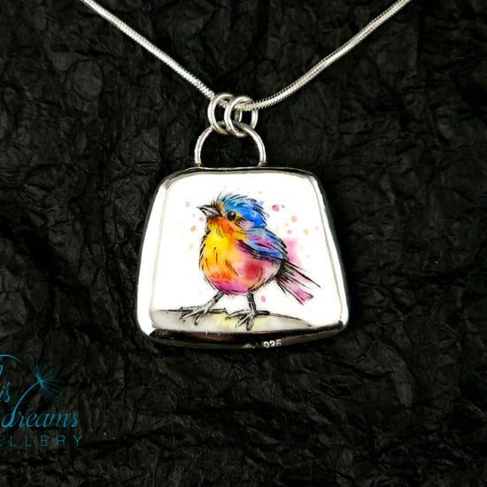 Handmade sterling silver pendant featuring a handpainted bird on a reclaimed porcelain fragment, with bright, joyful enamel colours and elegant silver frame